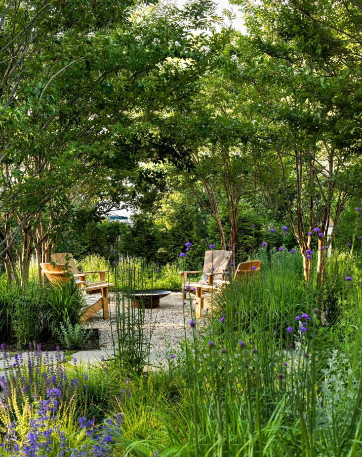 The firepit area is almost completely concealed by the surrounding circle of crepe myrtles when they are in leaf. The firepit is a 36-inch carbon steel model from the brand Fire Pit Art. The teak chairs are the Douglas Nance Santa Fe Adirondack Chairs.