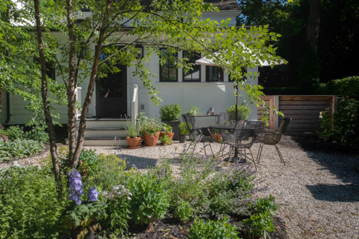 The driveway leads to the back of the house, and the entry more often used by the couple, where garden beds create outdoor rooms, including an outdoor dining room for summer meals, tucked between the flowers.