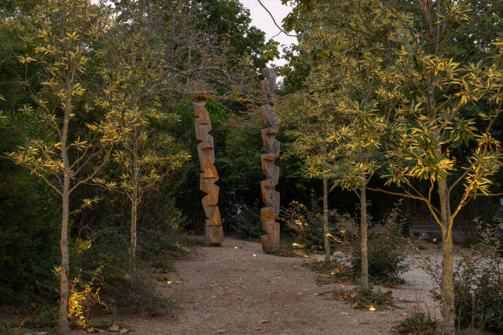  At the back of the property, Anna and Emilia planted a loose allée of native single stem Magnolia virginiana ‘Green Shadow’ trees, leading to a wood sculpture. “This space was intended to have a slightly more formal feeling from the front of the property with fewer plantings and more stone dust,” says Emilia. Photograph courtesy of Nick and Christina Martin.