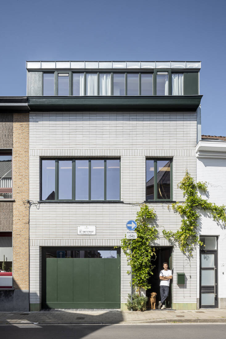 Arthur and their dog posing at the front door of their remodeled row house. Two simple changes to the exterior transformed the entire look: \1) painting the new garage door, gutter, and window frames green and \2) adding a wisteria to frame the front door.