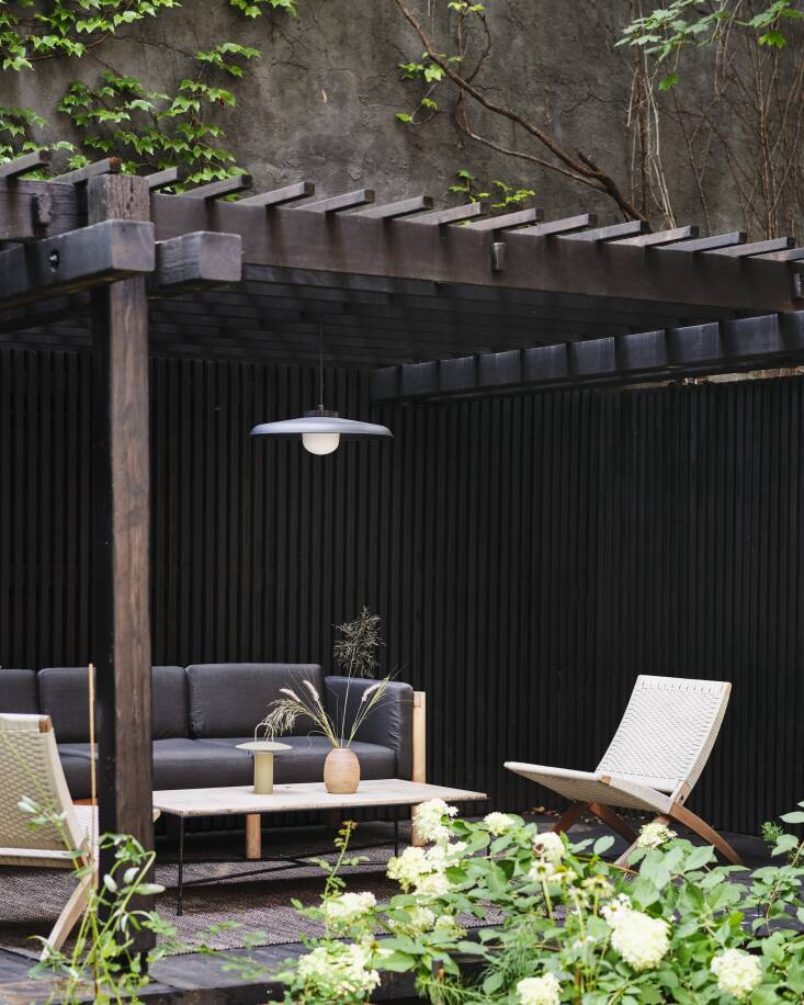 A Hoist Pendant by RBW hangs over the raised outdoor living room (to the left is the dining space). The MG50\1 Cuba Lounge Chairs are by Carl Hansen & Son; the Haven Sofa is by Neighbor; and the Pavilion Coffee Table by Paul McCobb is a CB\2 reissue.